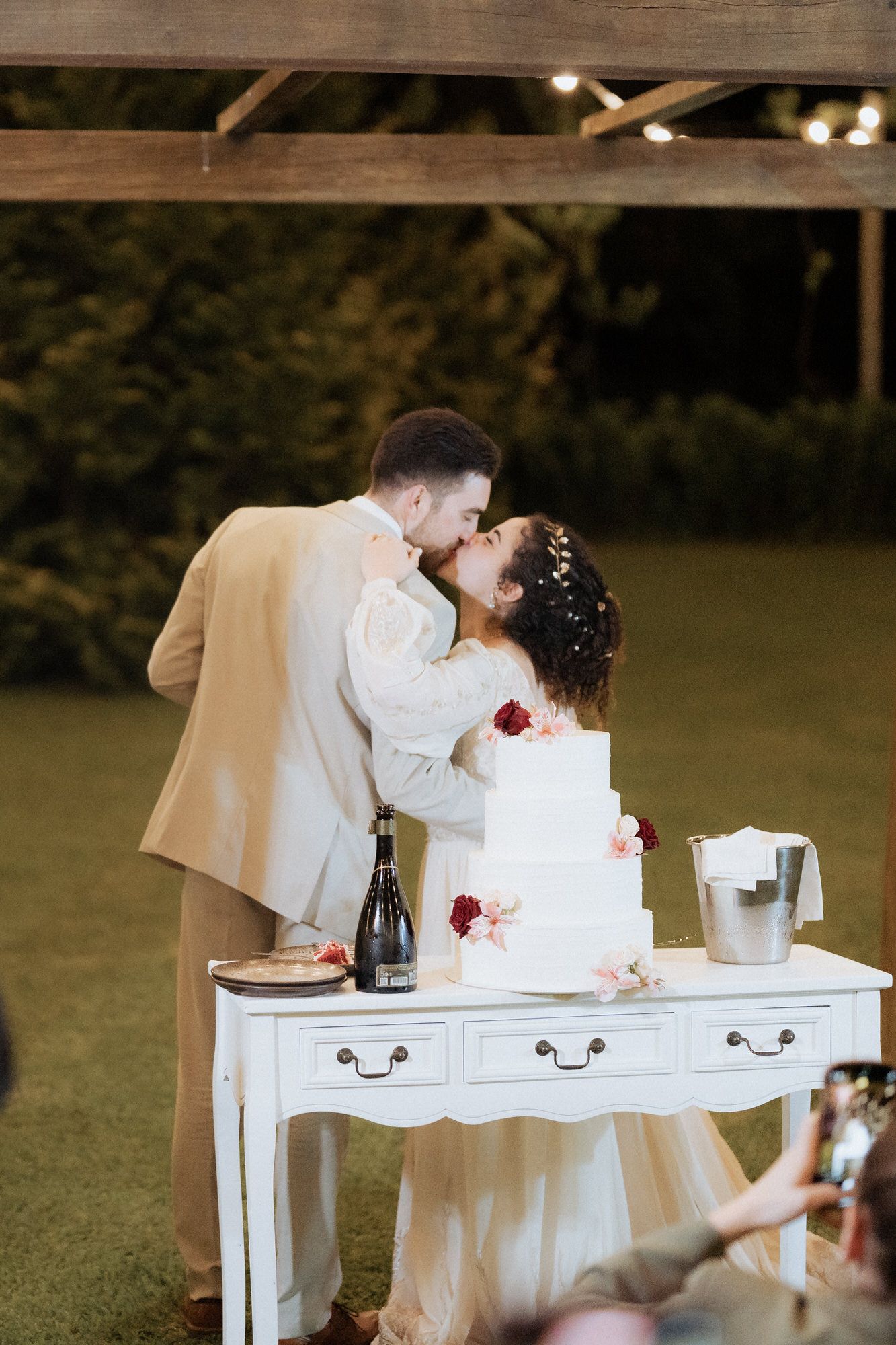 A romantic wedding couple shares intimate moments at a vintage white desk during their outdoor wedding reception.