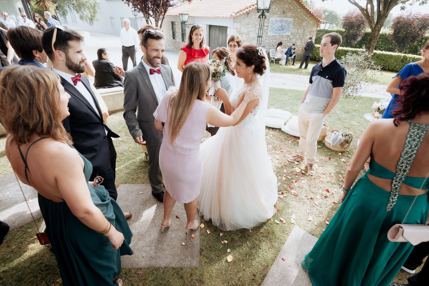 Wedding guests gather outdoors to greet and celebrate with the happy couple during a sunny garden reception.