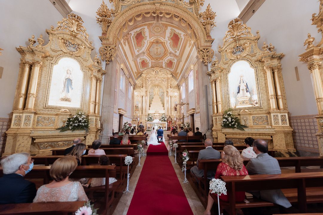 Ornate baroque church interior with gold columns and decorations along a red carpeted aisle during a ceremony.