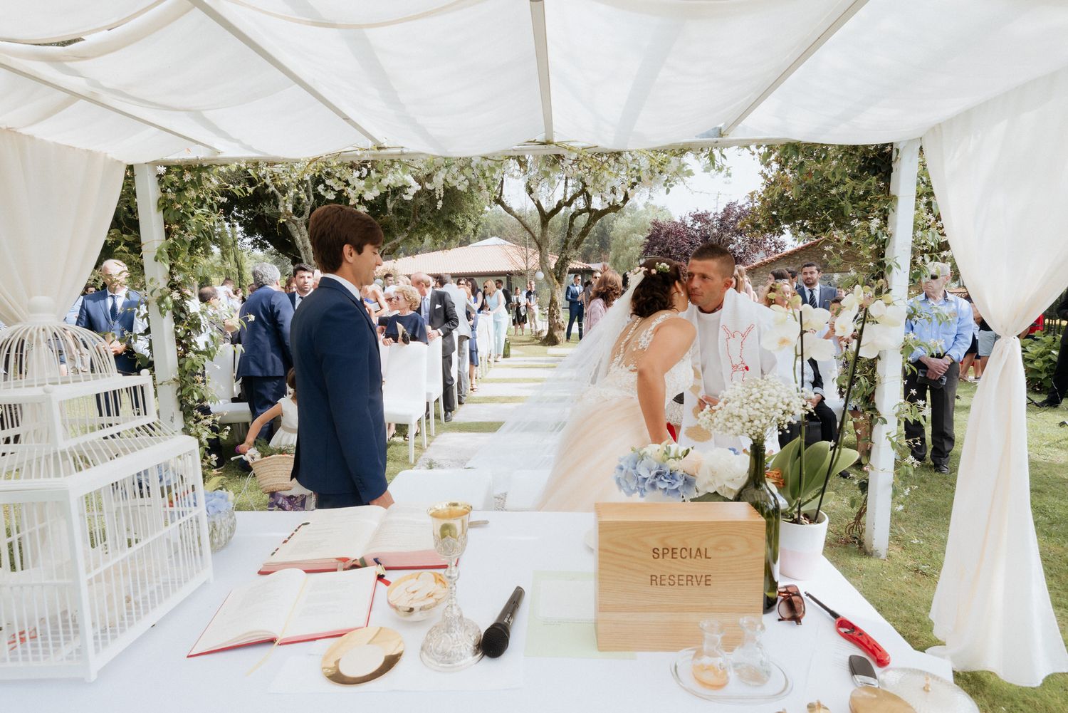 Rustic outdoor wedding reception setup with white birdcages and fabric canopy in a garden setting.