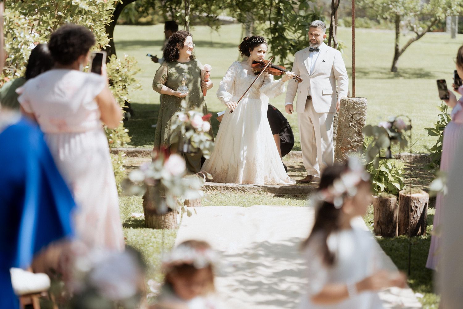 Elegant outdoor wedding ceremony under trees with white chairs and decorations on a sunny afternoon.