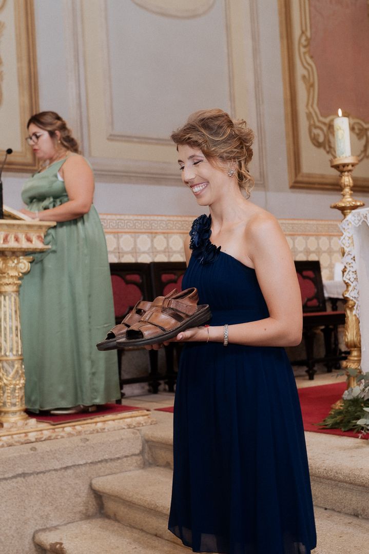 Two people in formal dresses at an elegant venue, with a bridesmaid in sage green and navy blue gowns near stairs.