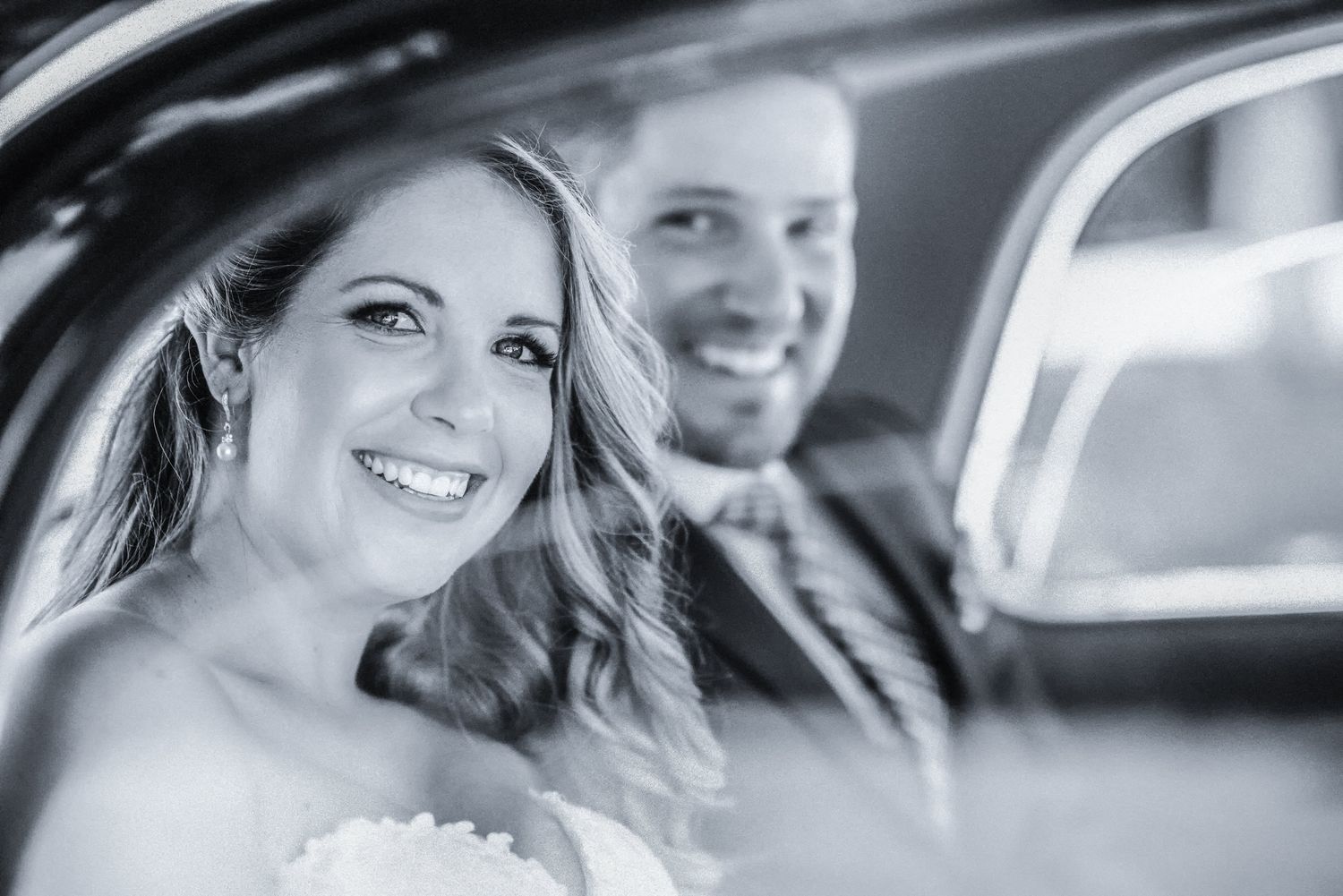 Recém-casados compartilham um momento alegre dentro de um carro clássico.