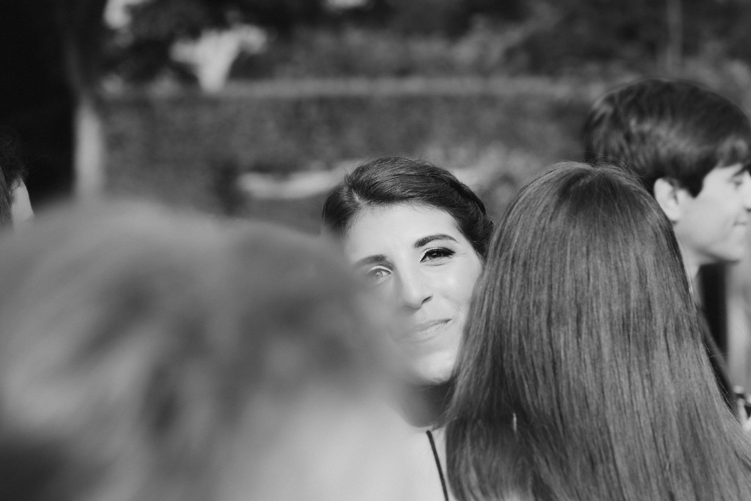 A black and white candid photograph shows someone smiling in a crowd while looking to the side.