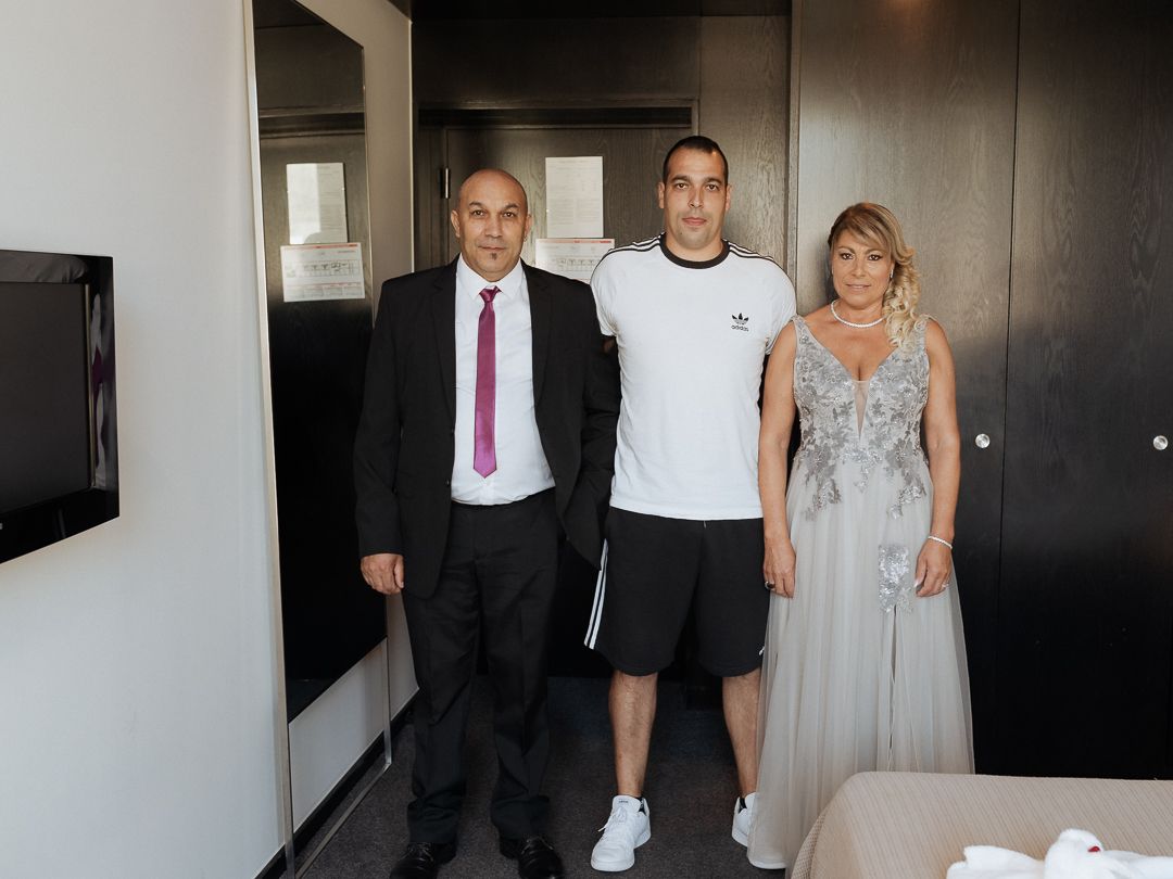 Three people pose together in a hotel room interior, with formal attire and casual athletic wear.