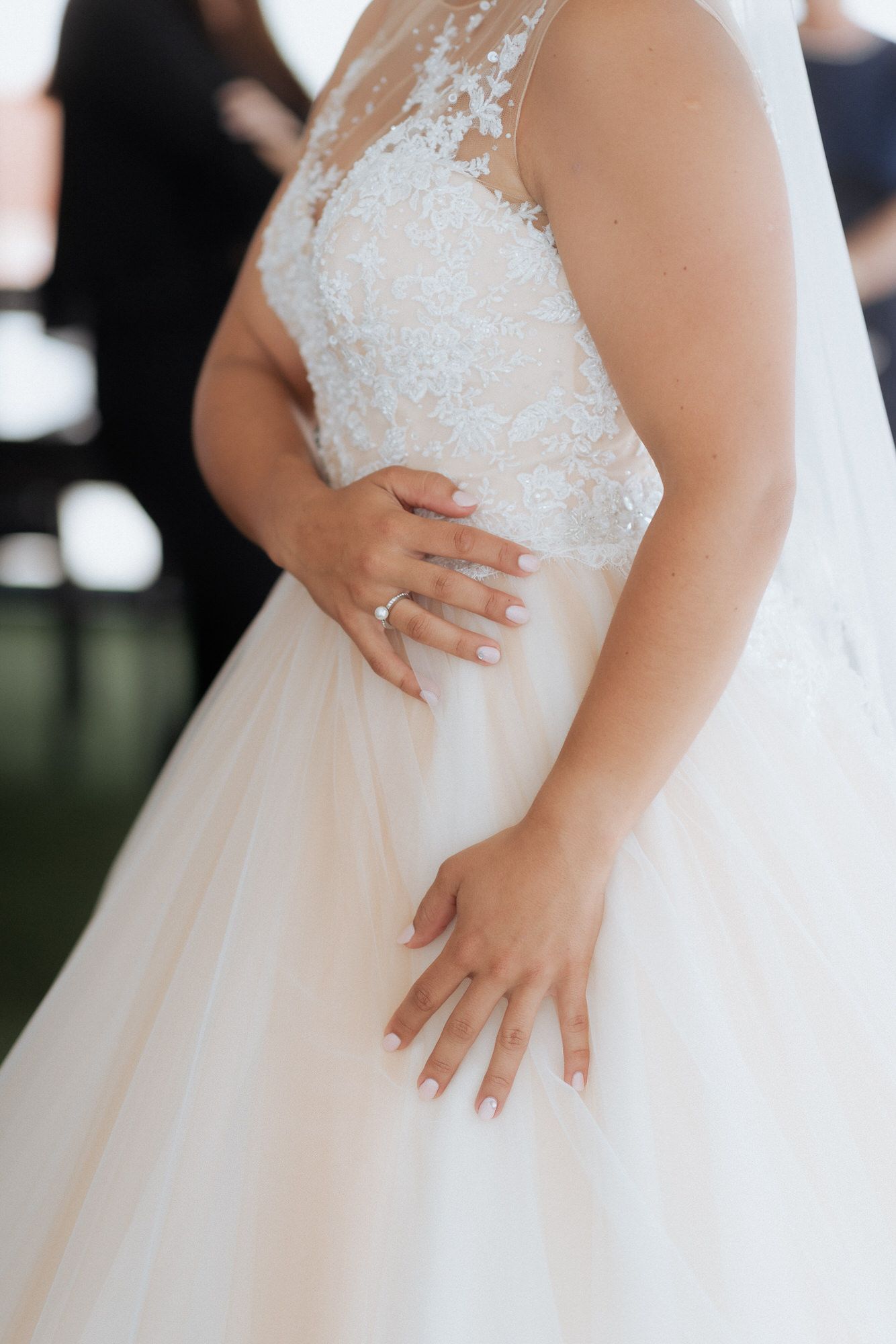 Close-up view of a bride wearing a white tulle wedding gown with lace bodice detailing and freshly manicured hands.