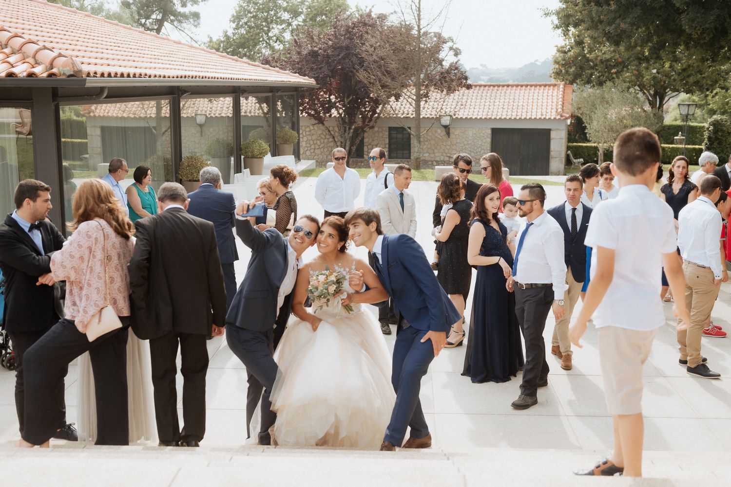 Wedding guests gather outdoors at a venue with Spanish tile roofs as newlyweds share a celebratory moment.
