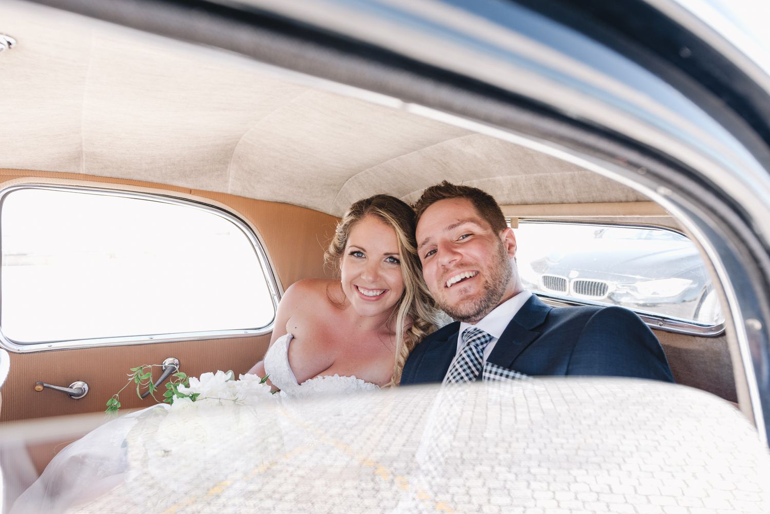 A joyful wedding couple shares a moment together in the backseat of a classic car.