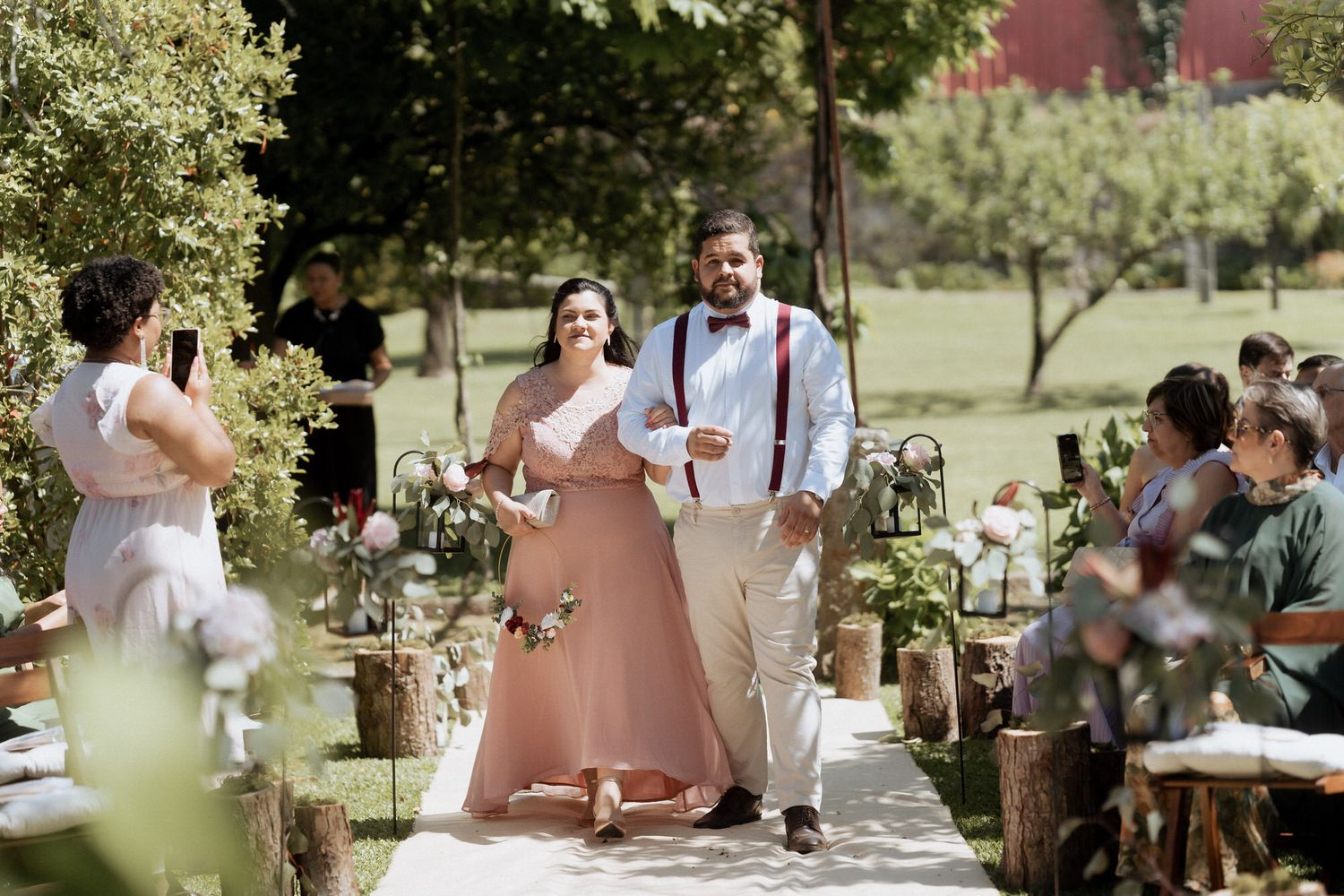 A sunny outdoor wedding ceremony with rustic decor and guests gathered in a garden setting.