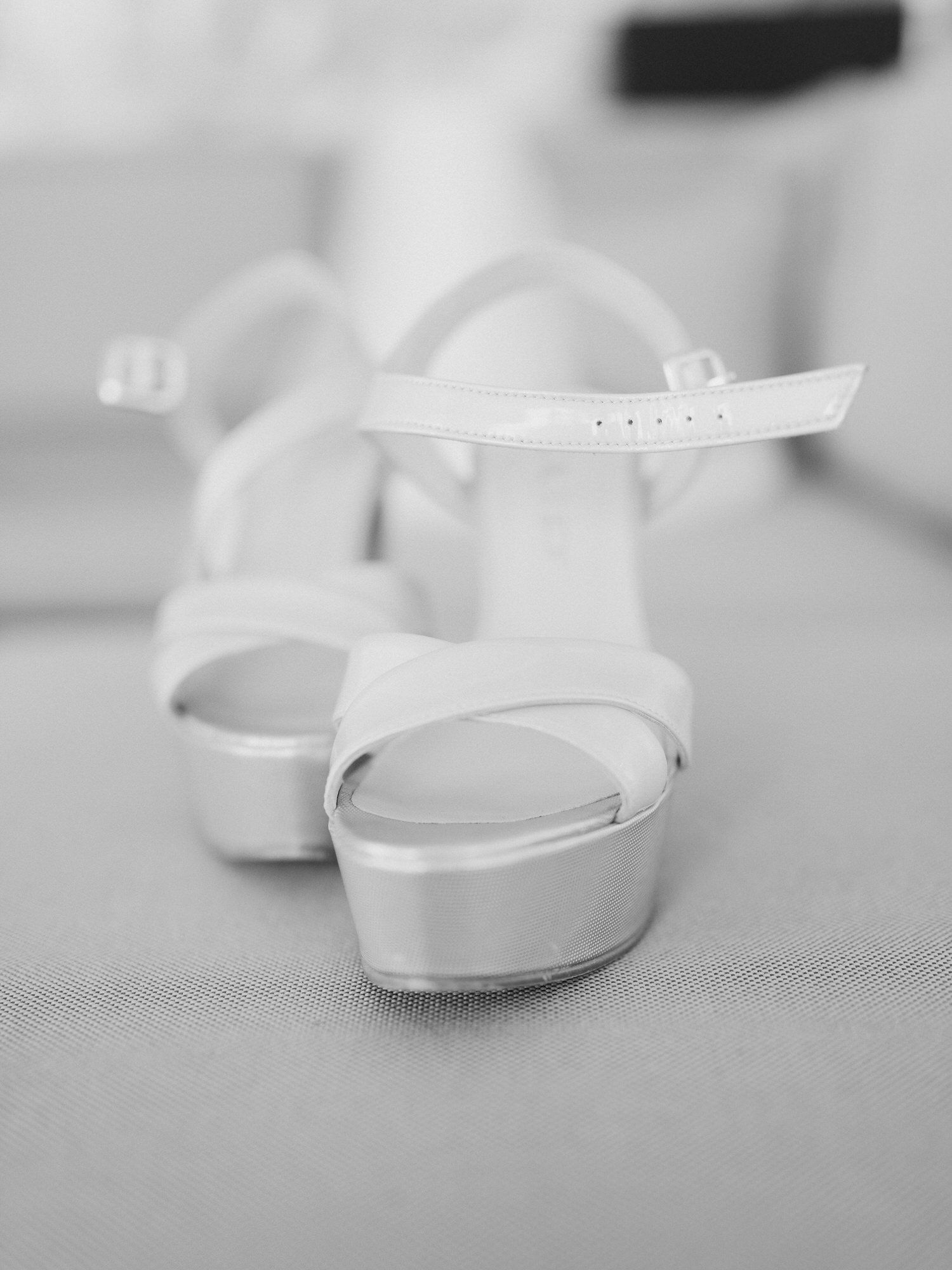 A pair of elegant white platform sandals with ankle straps photographed in black and white.