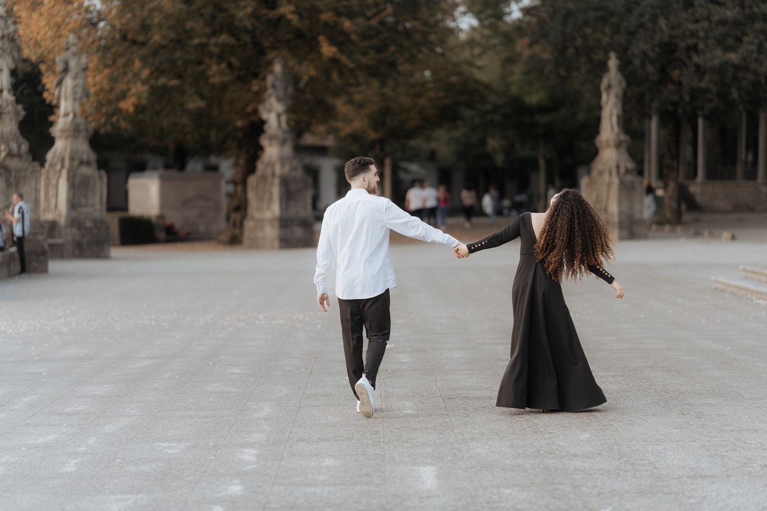 Um casal em trajes contrastantes de branco e preto dançando junto em um caminho arborizado.