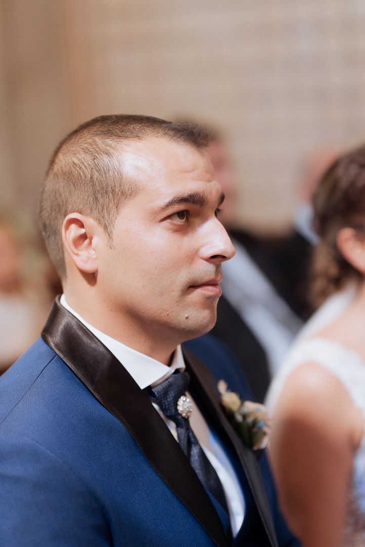 A formal event attendee in a navy blue tuxedo with black lapels and boutonniere stands in profile.