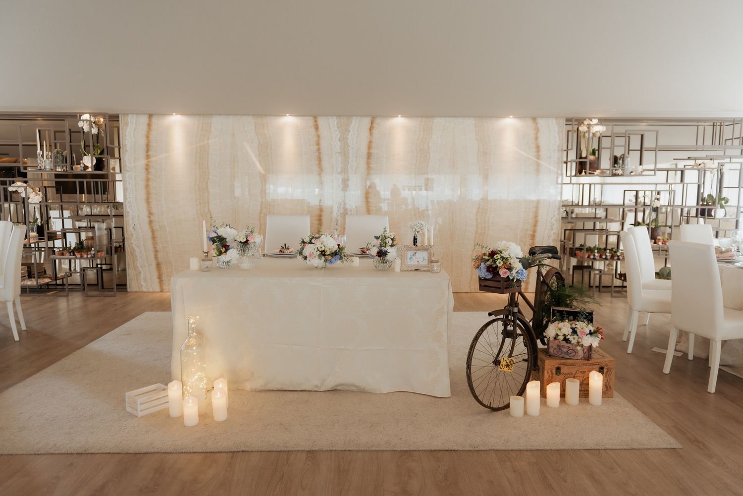 An elegant wedding reception setup with a head table, candles, and vintage bicycle decoration in a modern white venue.