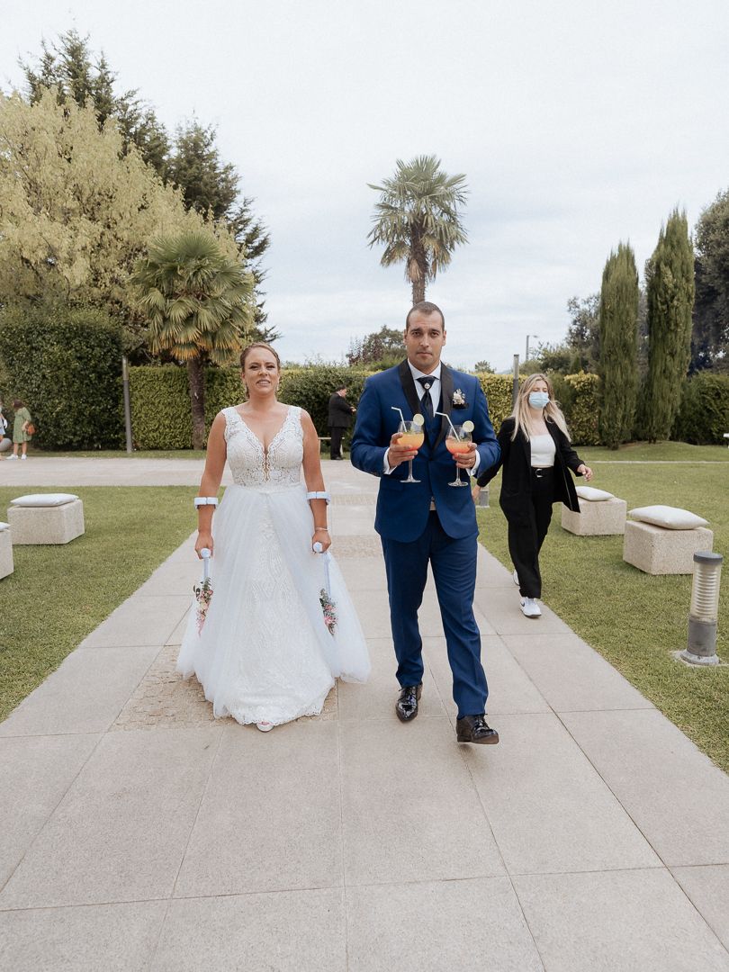 A couple in wedding attire walks down an outdoor stone path lined with palm trees and greenery on their special day.