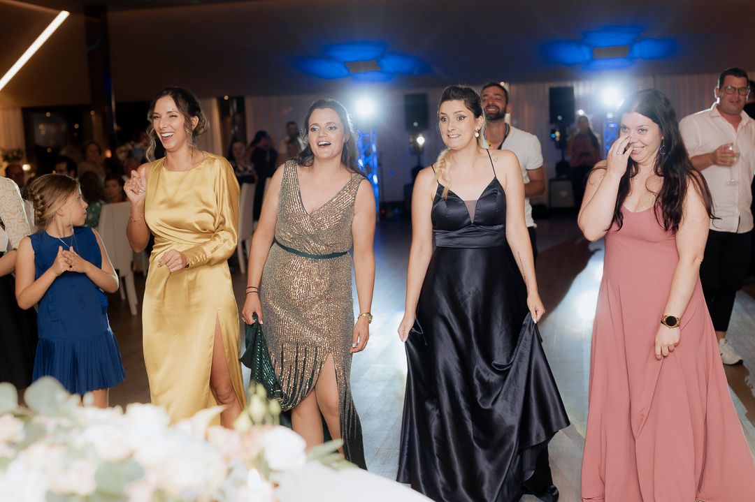 People in formal attire dancing and having fun at an elegant evening reception with blue lighting and floral decorations.