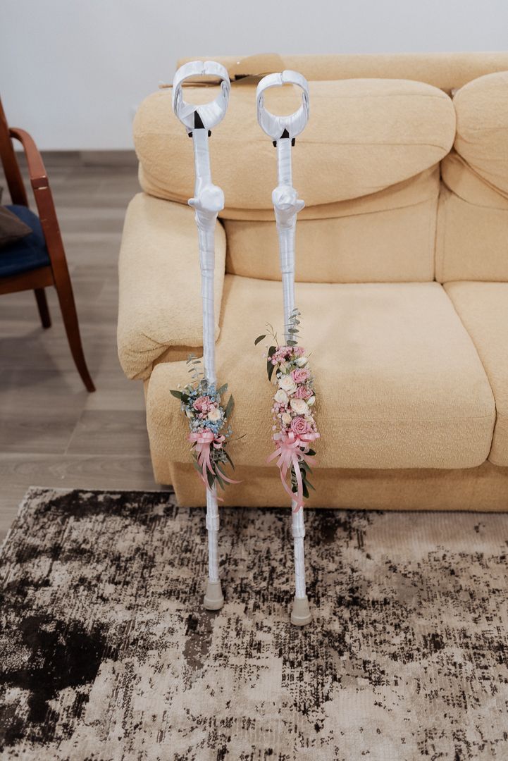 Two decorative white crutches adorned with delicate pink and purple floral arrangements rest against a beige couch.