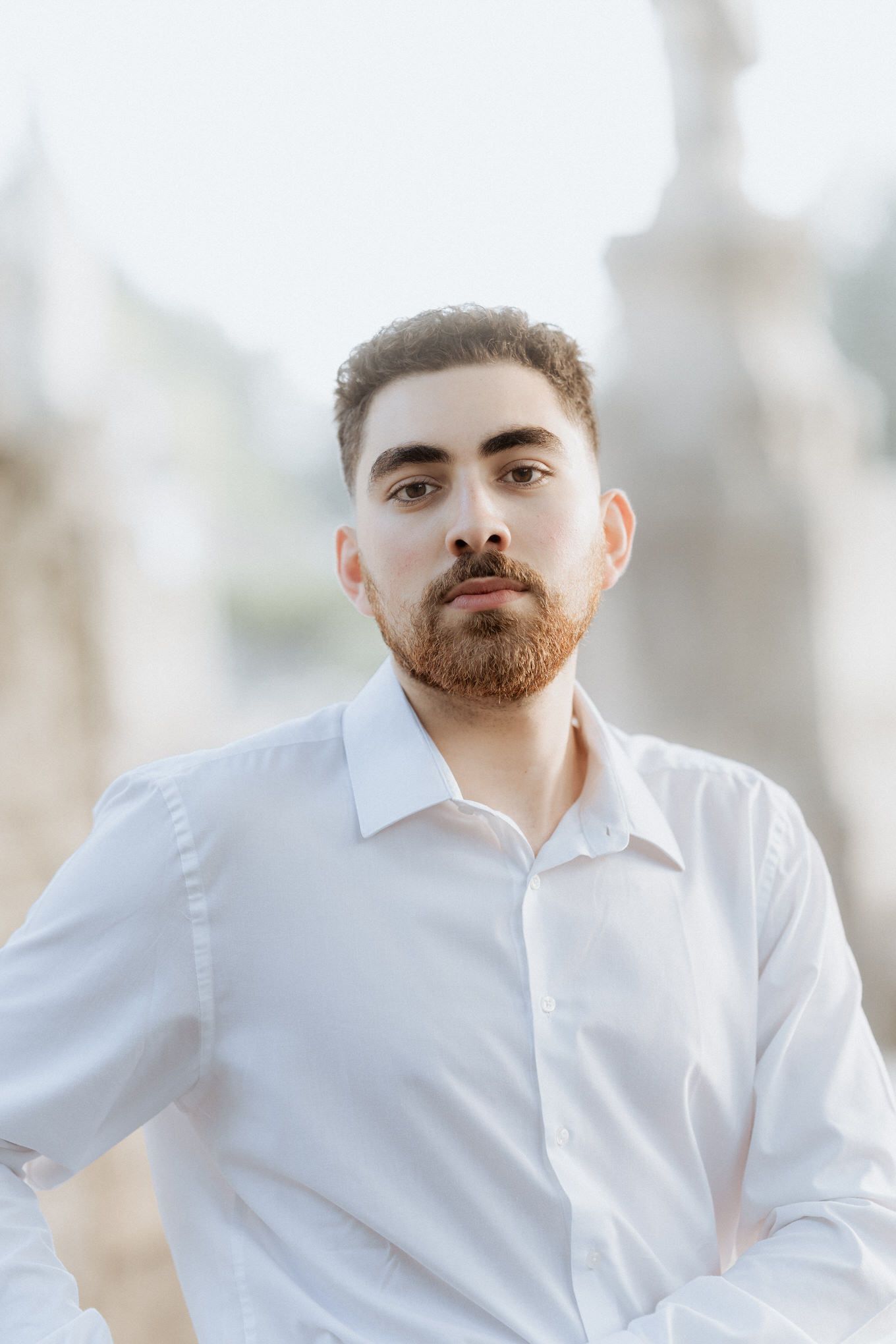 Retrato de namorado com camisa branca de botões, capturado com iluminação natural suave e fundo desfocado.
