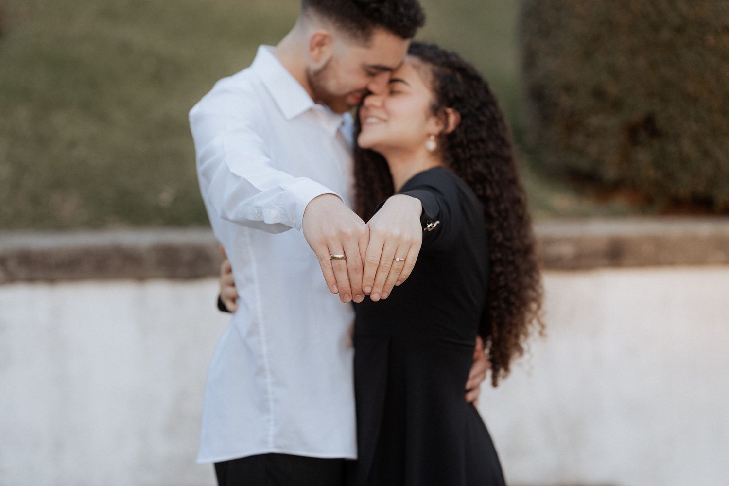Um casal se abraça enquanto exibe um anel de noivado brilhante em um fundo desfocado ao ar livre.