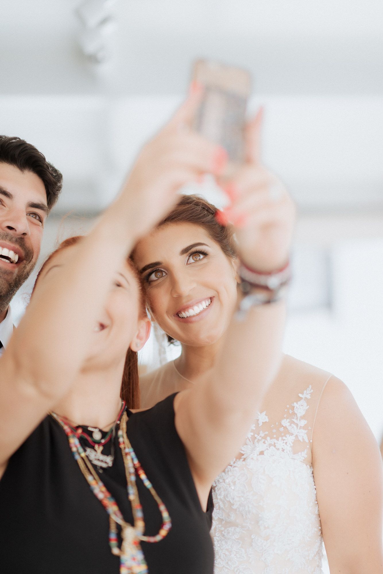 Couple taking cheerful selfie together at wedding celebration with bride wearing white lace dress.