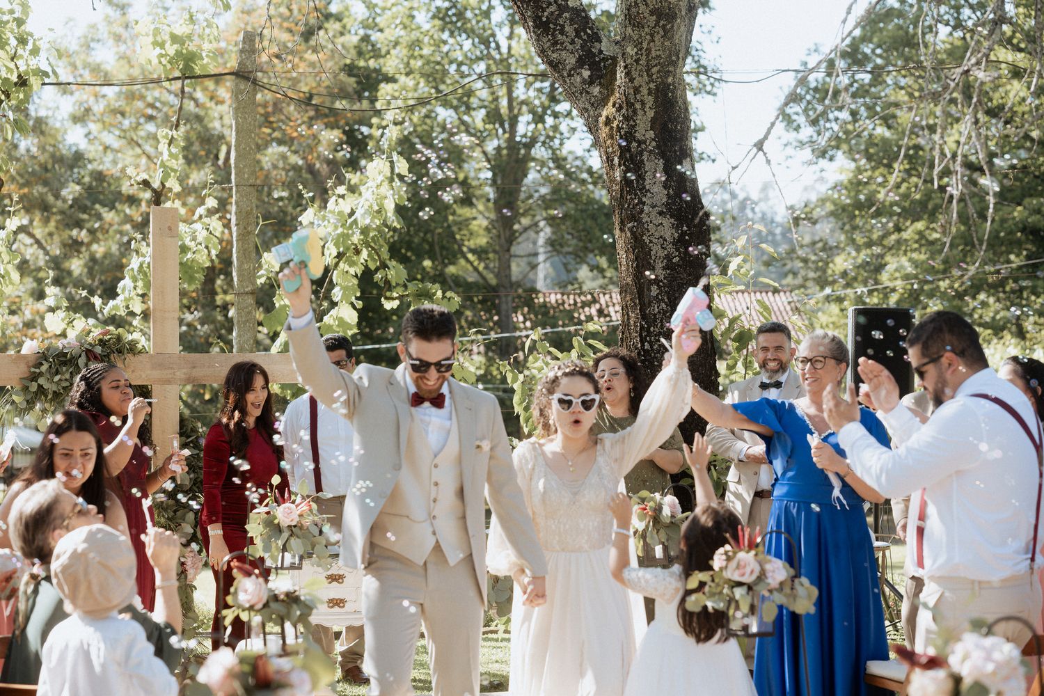 A joyful celebration at an outdoor garden wedding with bridal party in white, burgundy and blue attire.