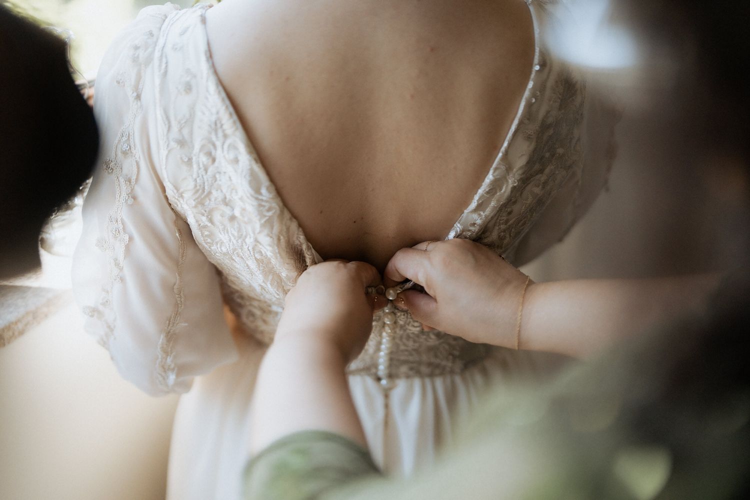 Close-up view of hands fastening delicate lace buttons on a white wedding dress.