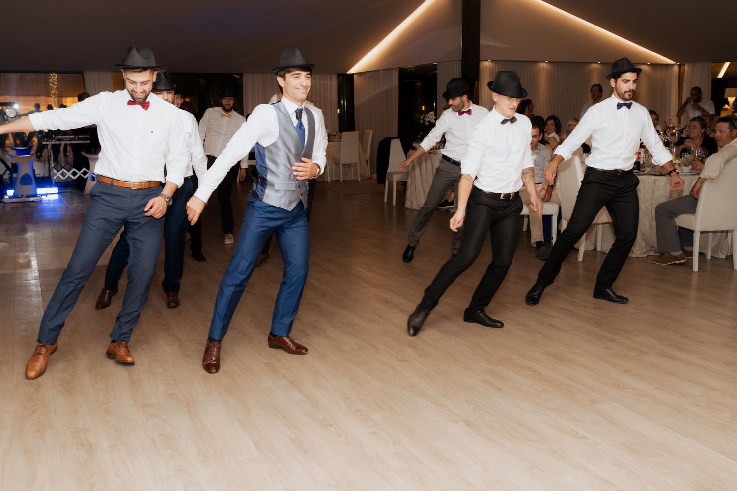 Groomsmen perform a synchronized dance routine at a wedding reception on a wooden dance floor.