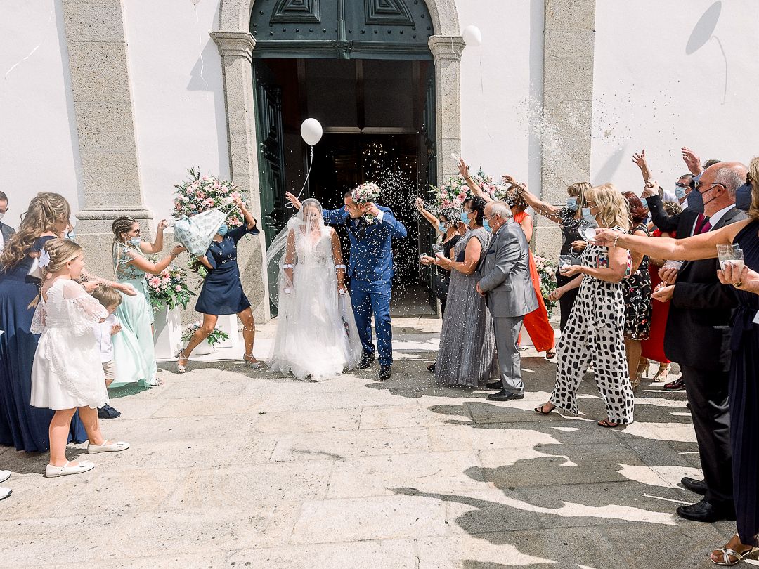Celebration outside a church building as newlyweds depart through a line of cheering guests throwing confetti.