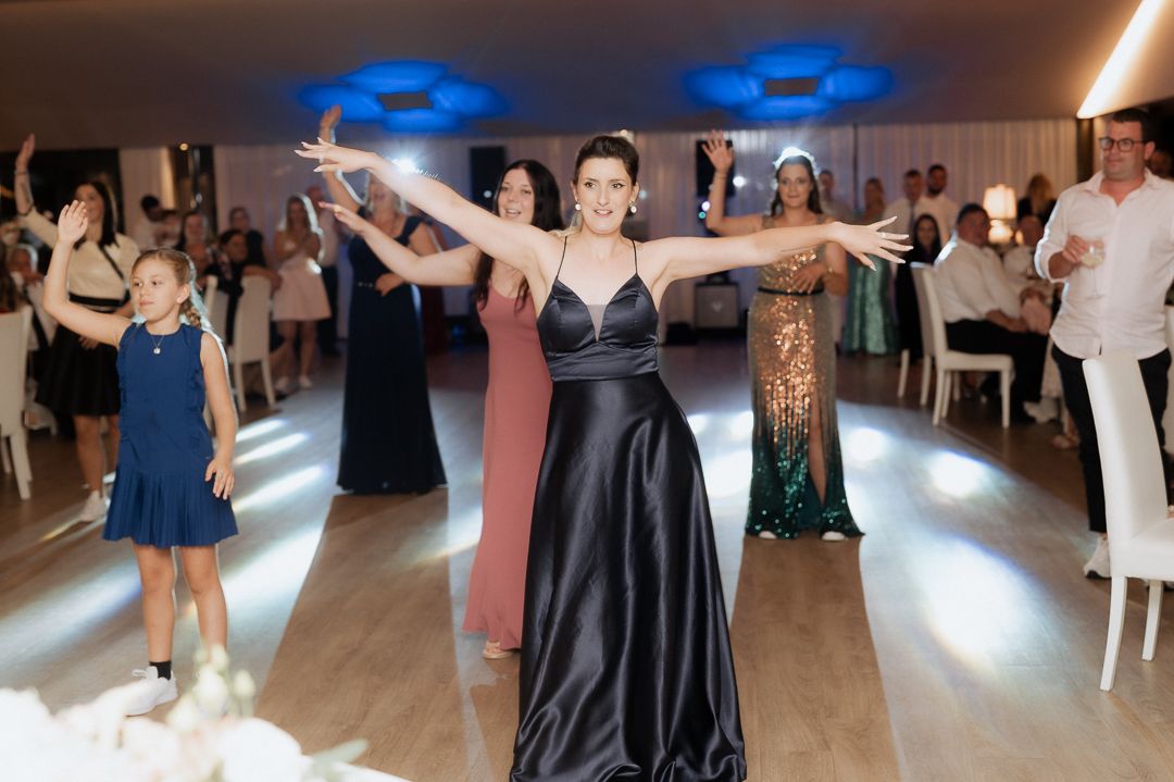 Dancers in formal evening wear celebrate on a wooden dance floor at an elegant event with blue lighting overhead.