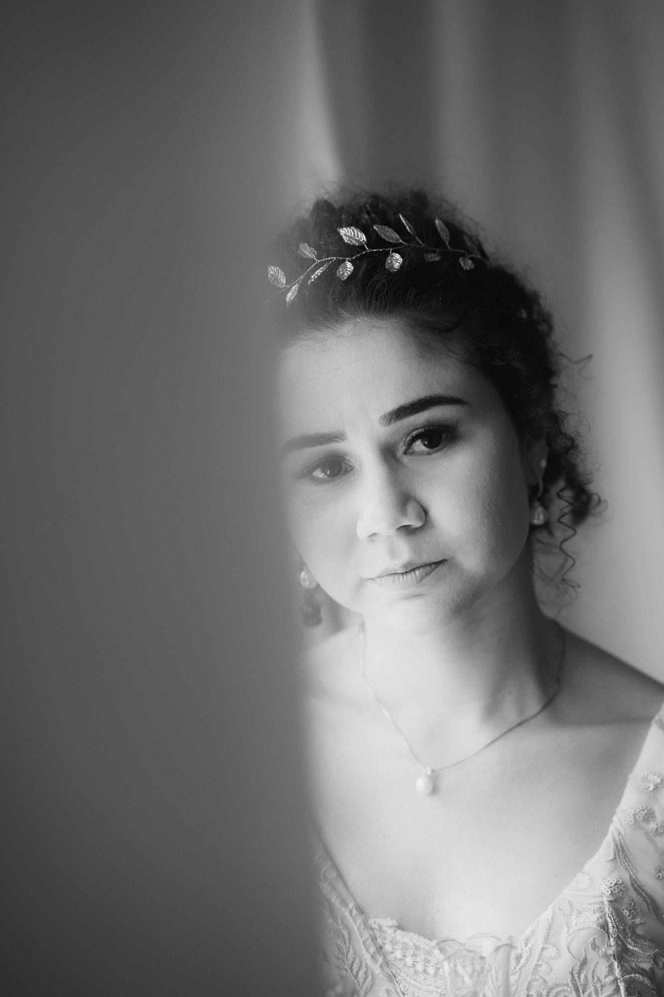 Black and white portrait showing a bride wearing delicate leaf hair accessories and lace gown in soft window light.