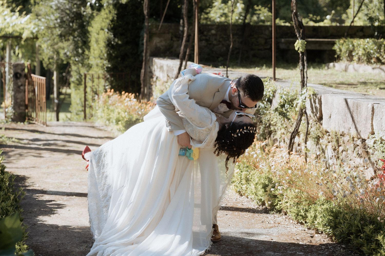 Two newlyweds share a romantic kiss while posing together outdoors on a beautiful garden pathway.