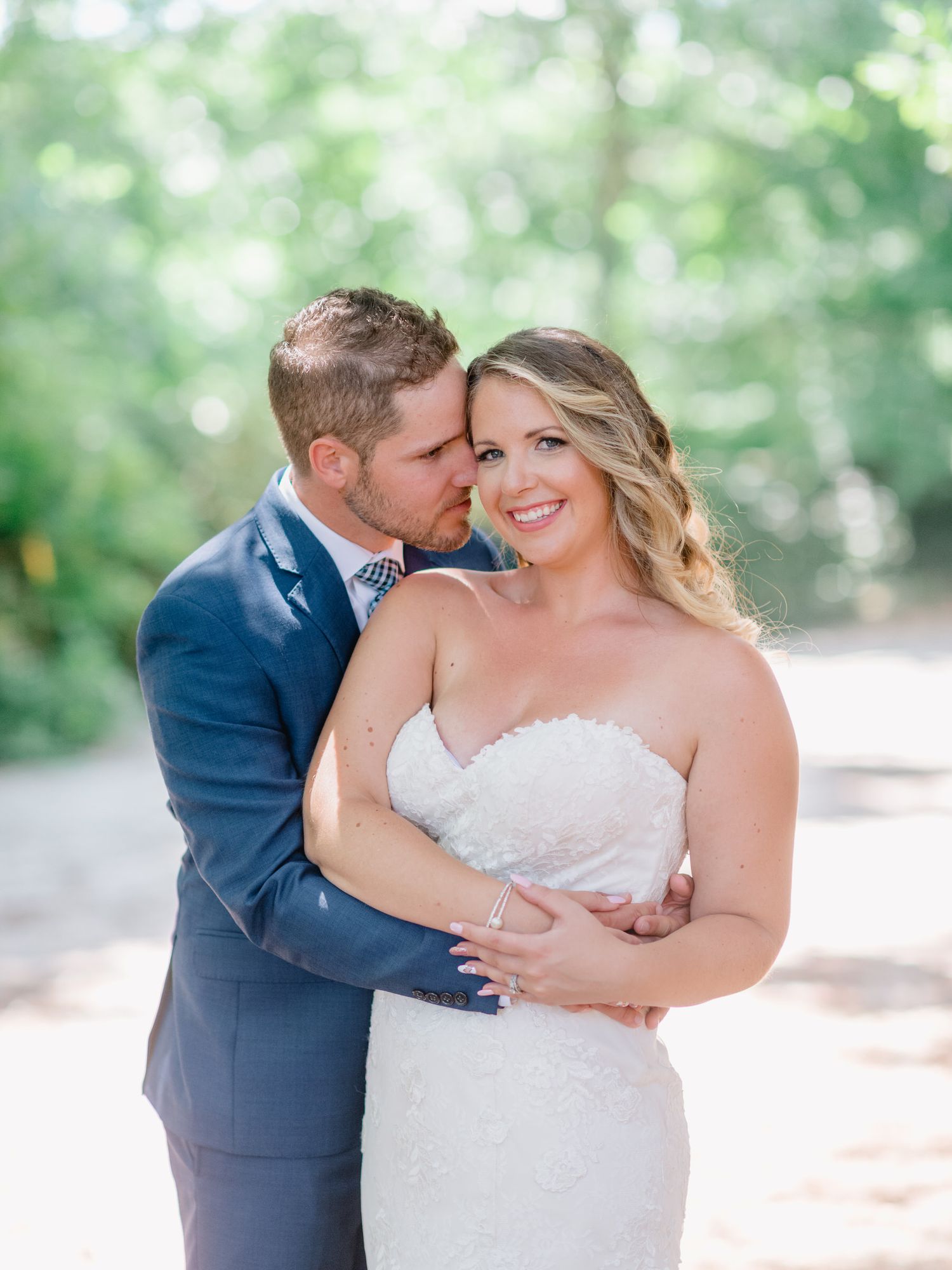 Retrato de casamento delicado com casal se abraçando contra um fundo desfocado de floresta.