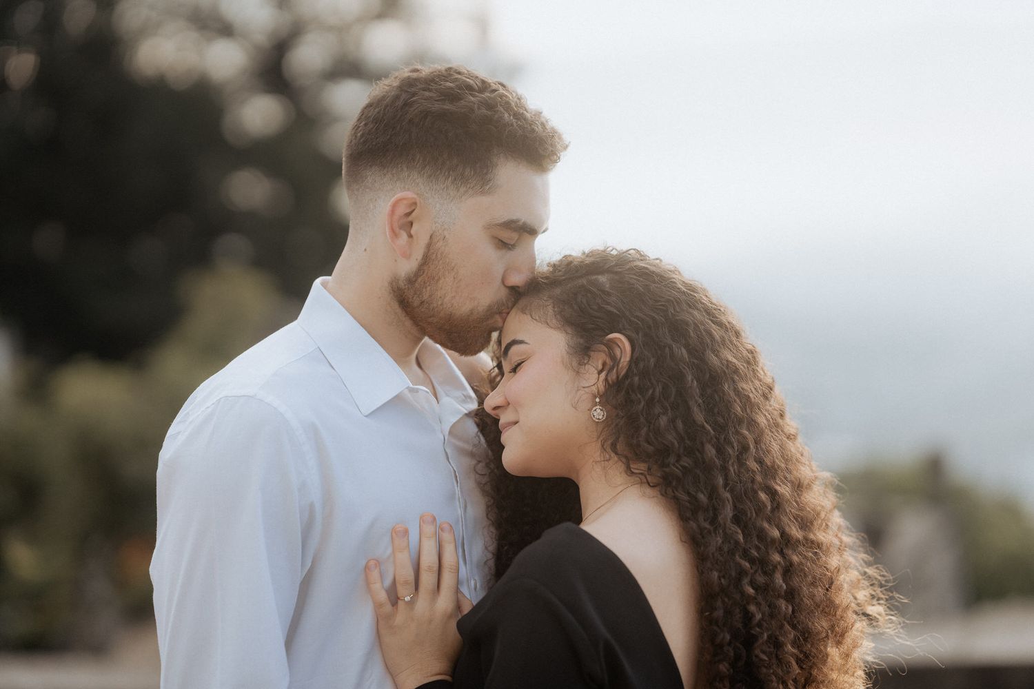 Um momento romântico e terno entre um casal se abraçando sob uma suave luz natural contra um fundo externo desfocado.