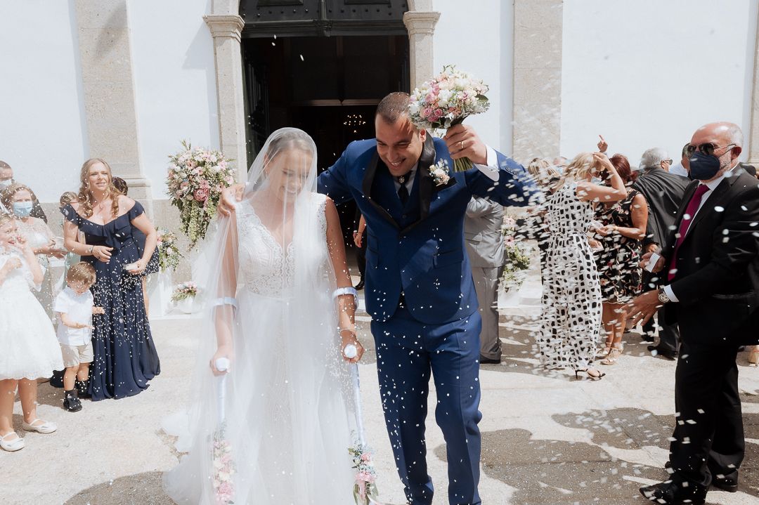 Wedding guests toss confetti while celebrating as a couple exits through an archway after their ceremony.