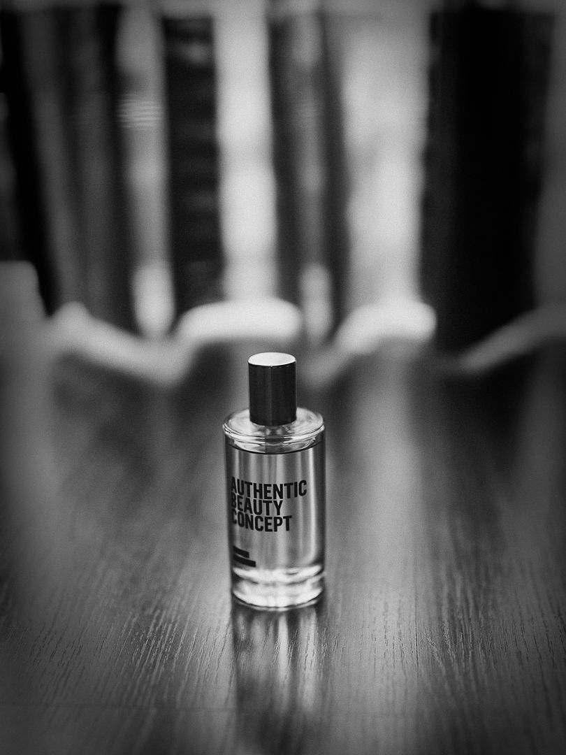 A glass perfume bottle labeled 'Authentic' sits on a dark wooden surface in black and white photography.