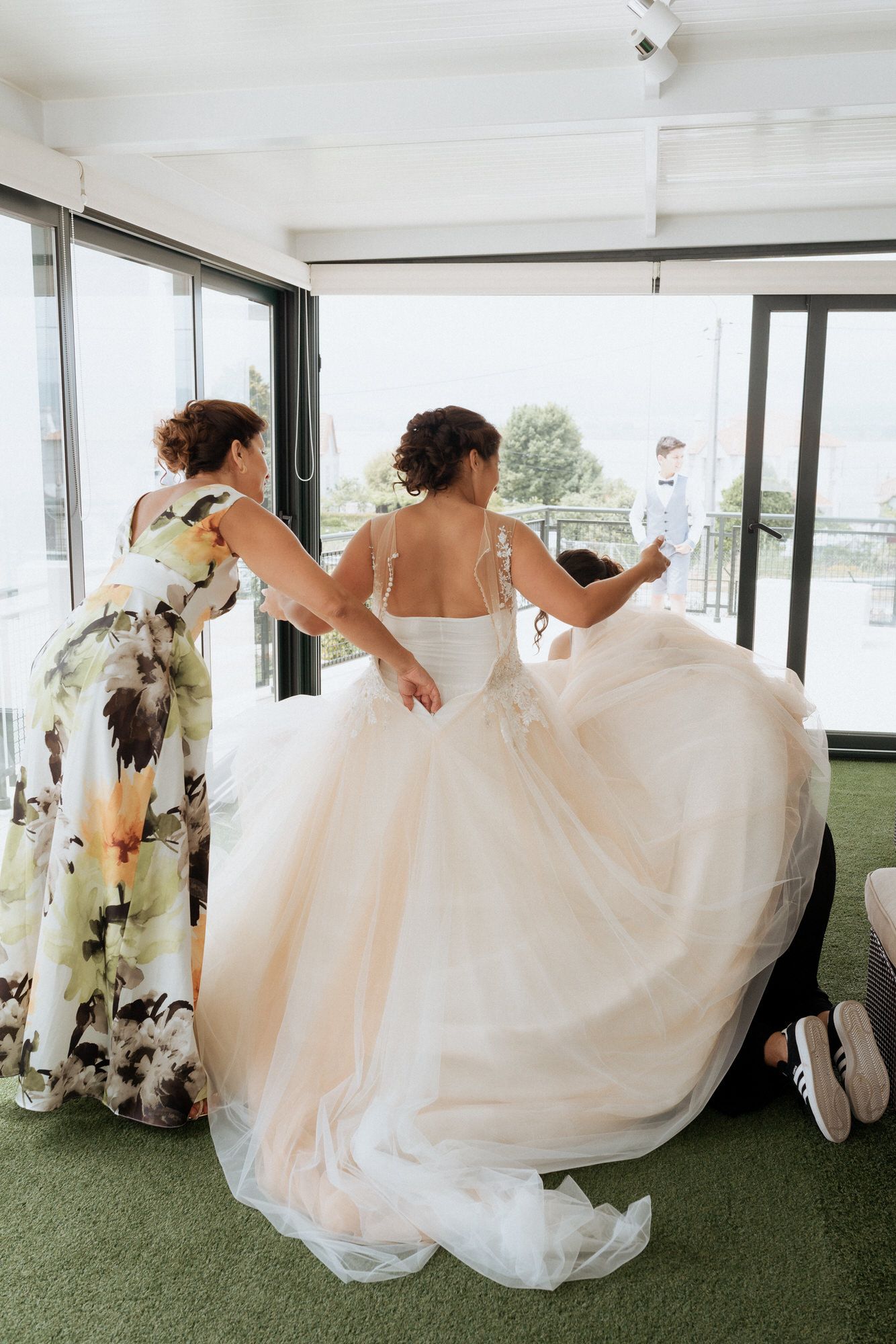 A group of wedding guests dressed in white gowns and floral dresses dive playfully through glass windows.