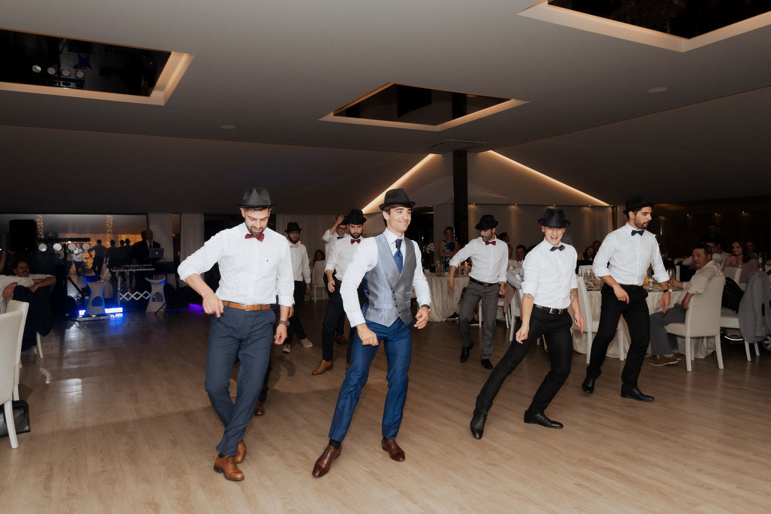 People dancing in a line formation on a wooden dance floor at an indoor event venue with modern lighting.