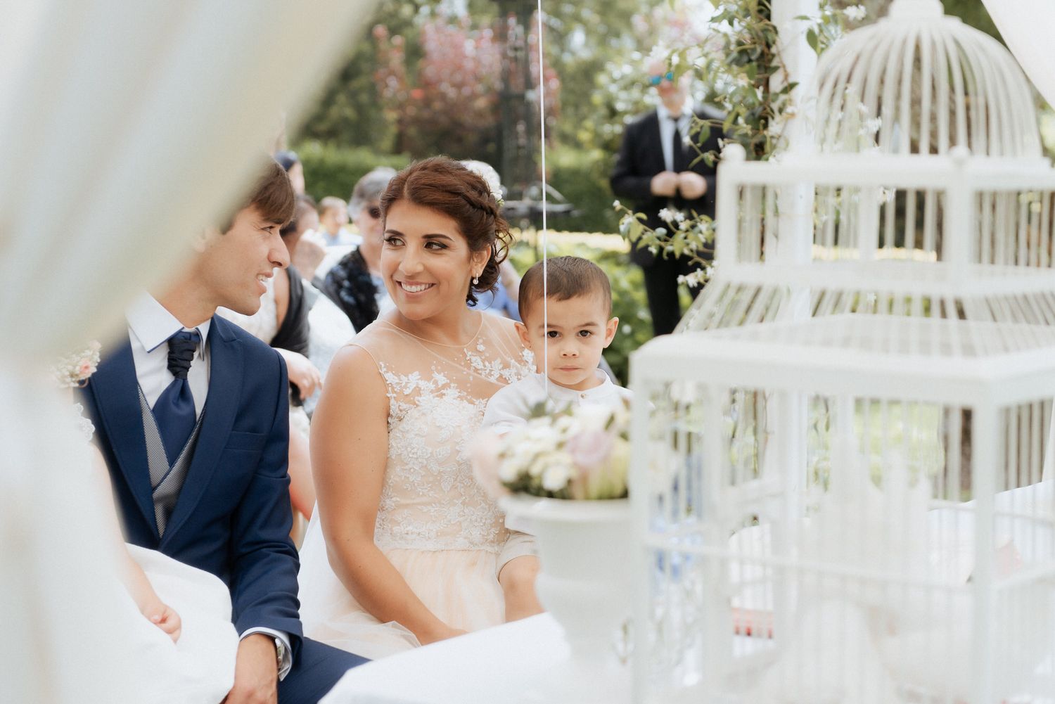 Wedding couple poses in a garden setting with decorative white birdcages and floral arrangements.