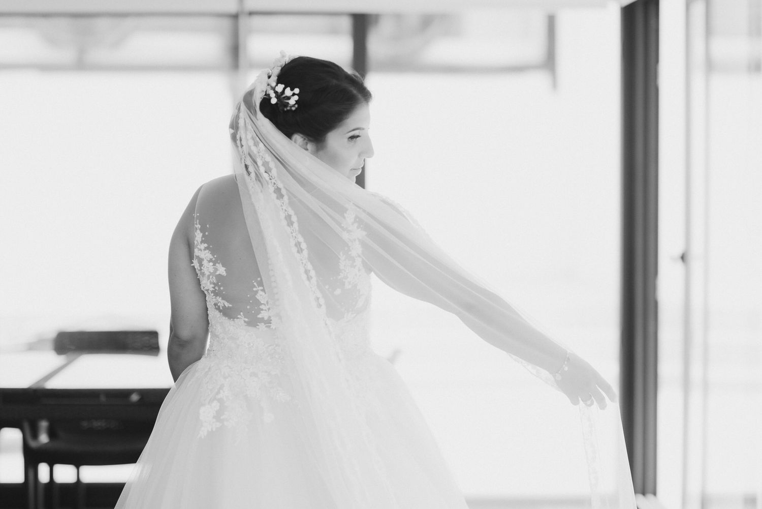 Black and white photo showing elegant bridal veil flowing behind a bride in a wedding dress, captured in soft focus.