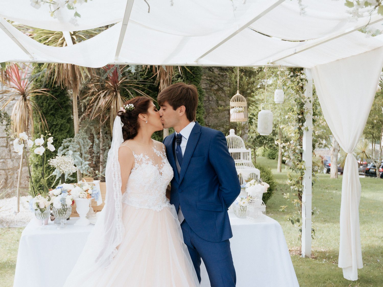 A couple shares an intimate moment under a white tent canopy during an elegant outdoor garden wedding celebration.