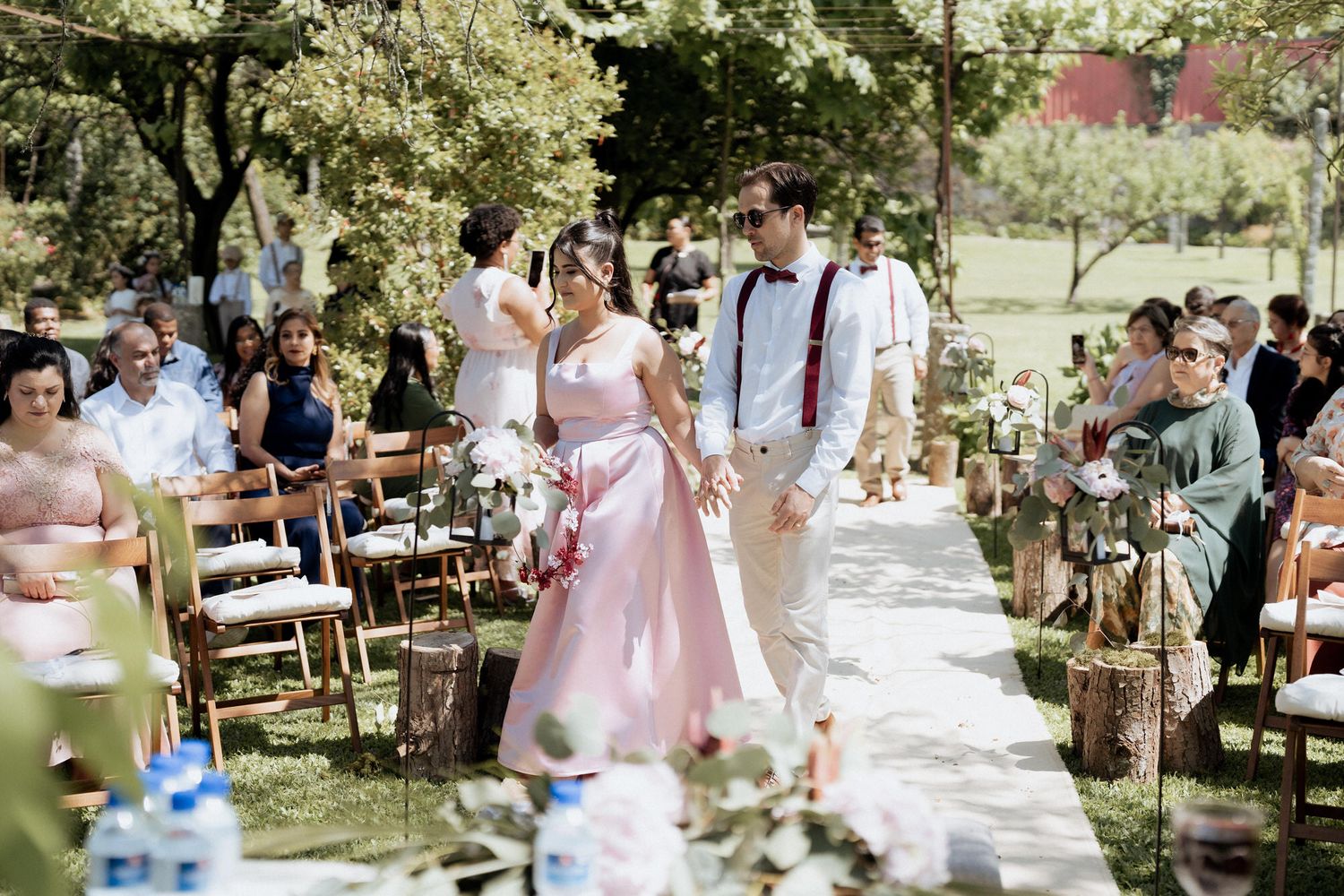 An outdoor garden wedding ceremony with wooden chairs lining a stone pathway decorated with delicate floral arrangements.