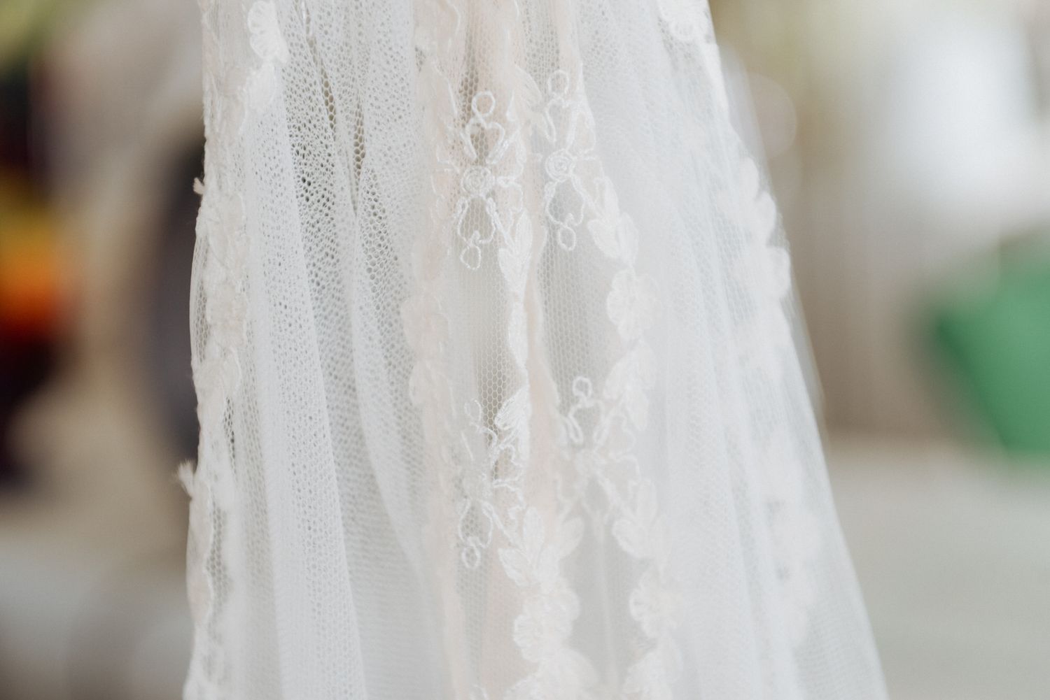 White lace wedding veil with delicate floral pattern details shown in soft focus against blurred background.