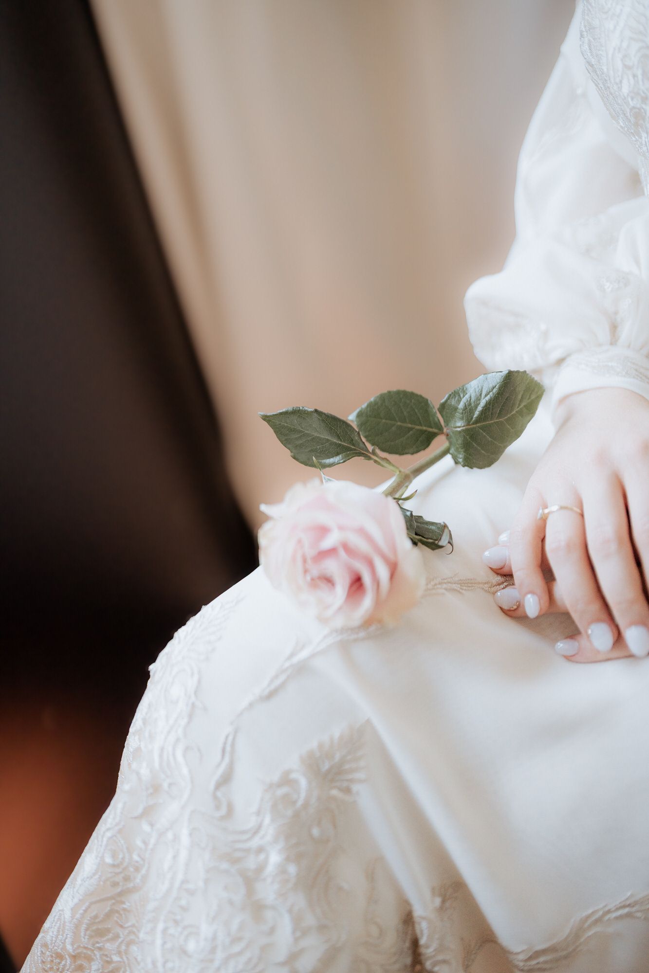 A delicate pink rose rests on white lace wedding dress fabric with intricate embroidery details.