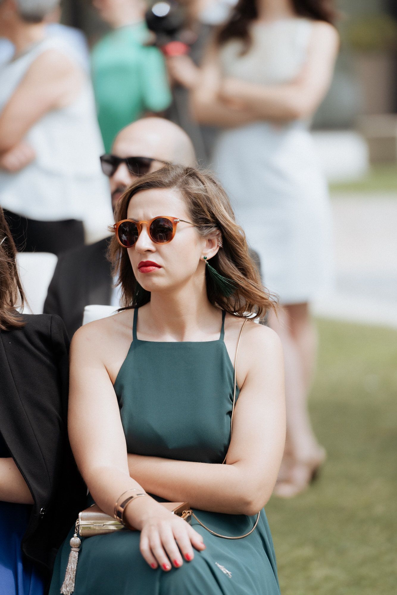 Person in a dark green sleeveless dress looking to the side while wearing sunglasses outdoors.