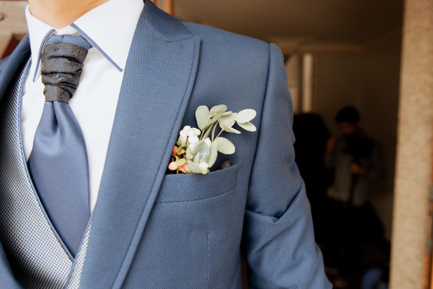 Wedding boutonniere with white flowers pinned to a navy blue suit lapel.