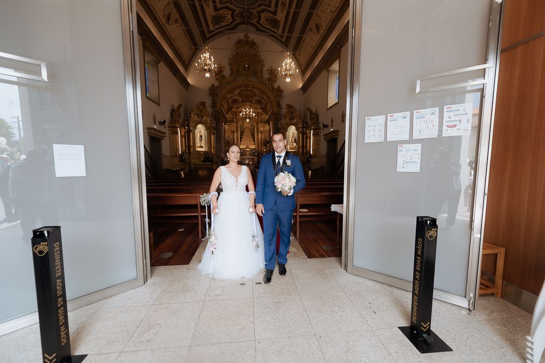 A couple walks down the aisle of an ornate church with vaulted ceilings, chandeliers and religious iconography.