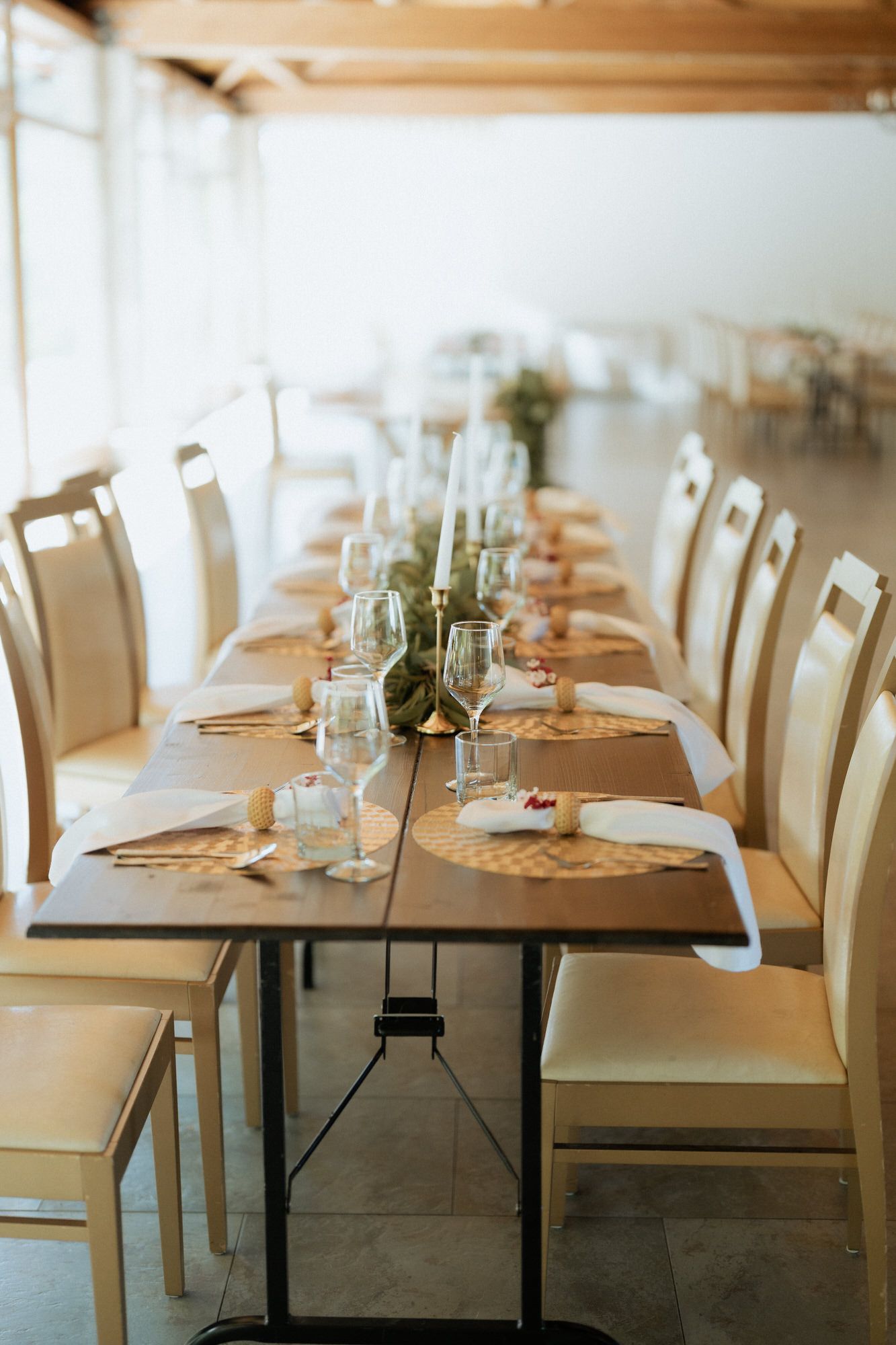 Long table setup for elegant dining with white chairs, place settings and minimalist centerpieces in natural light.