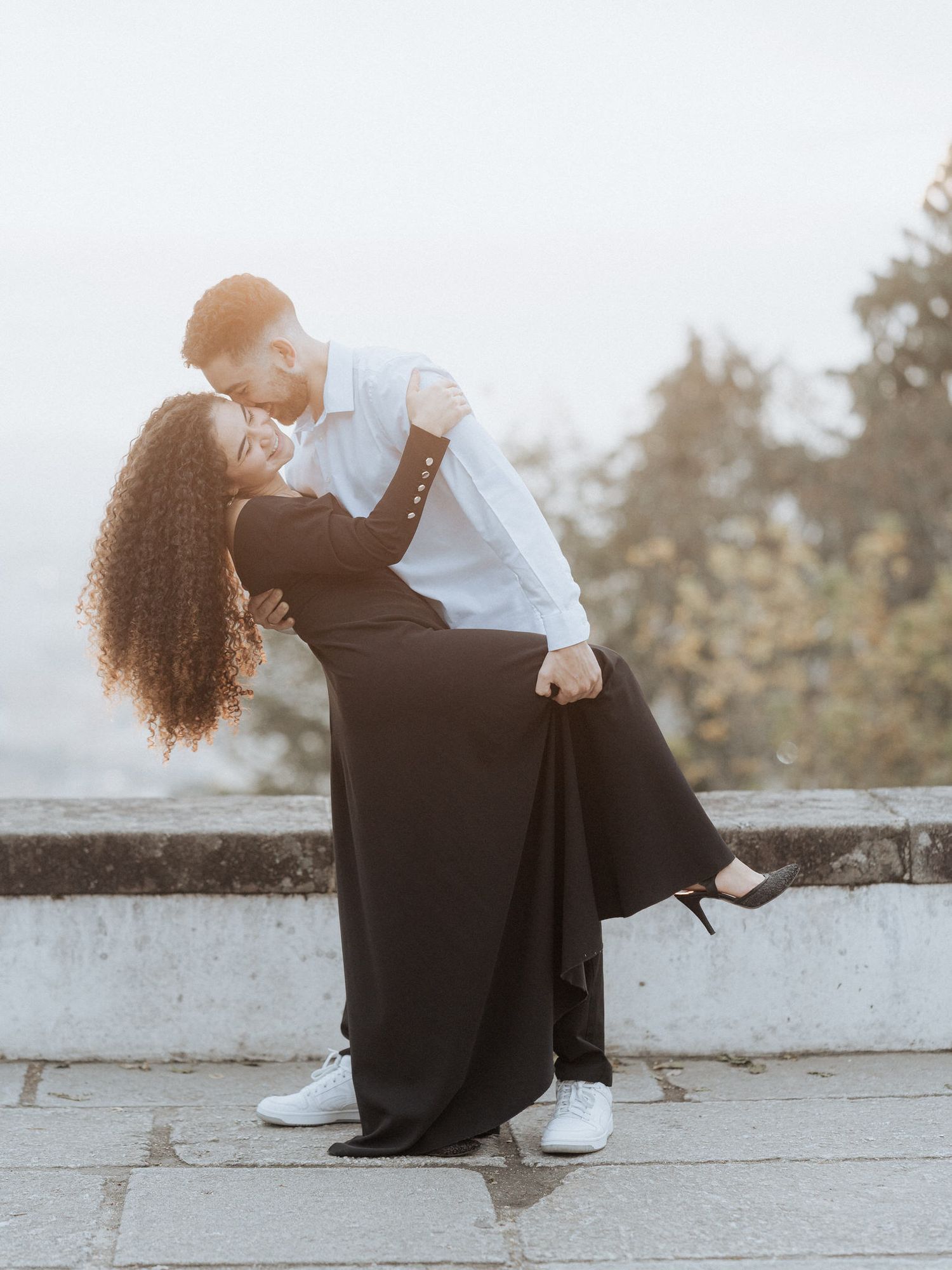 Um casal romântico em trajes contrastantes em preto e branco compartilha um momento íntimo sentado em um muro de pedra ao ar livre.