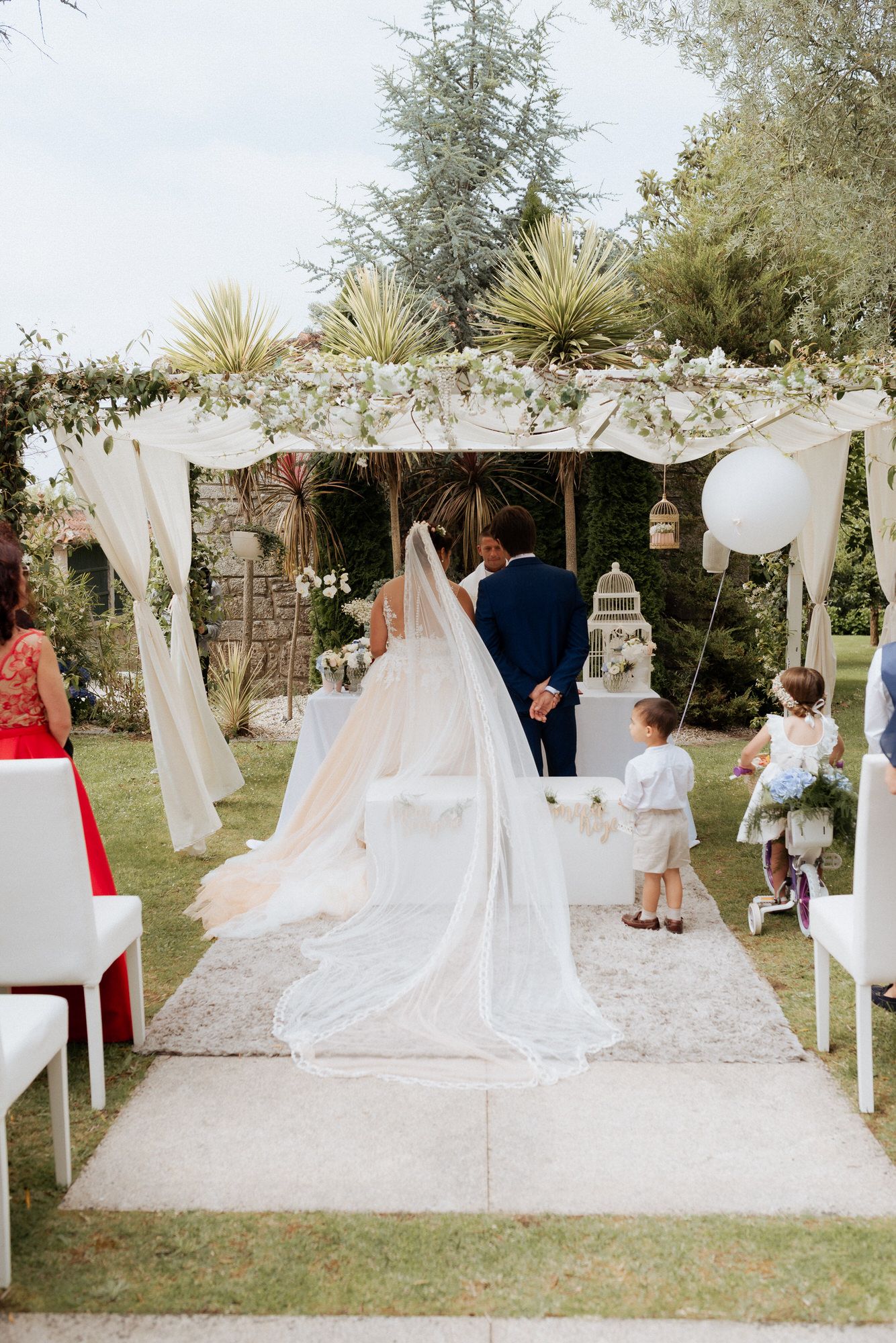 Outdoor wedding ceremony setup with white fabric draping along pathway creating elegant aisle walkway in garden setting.