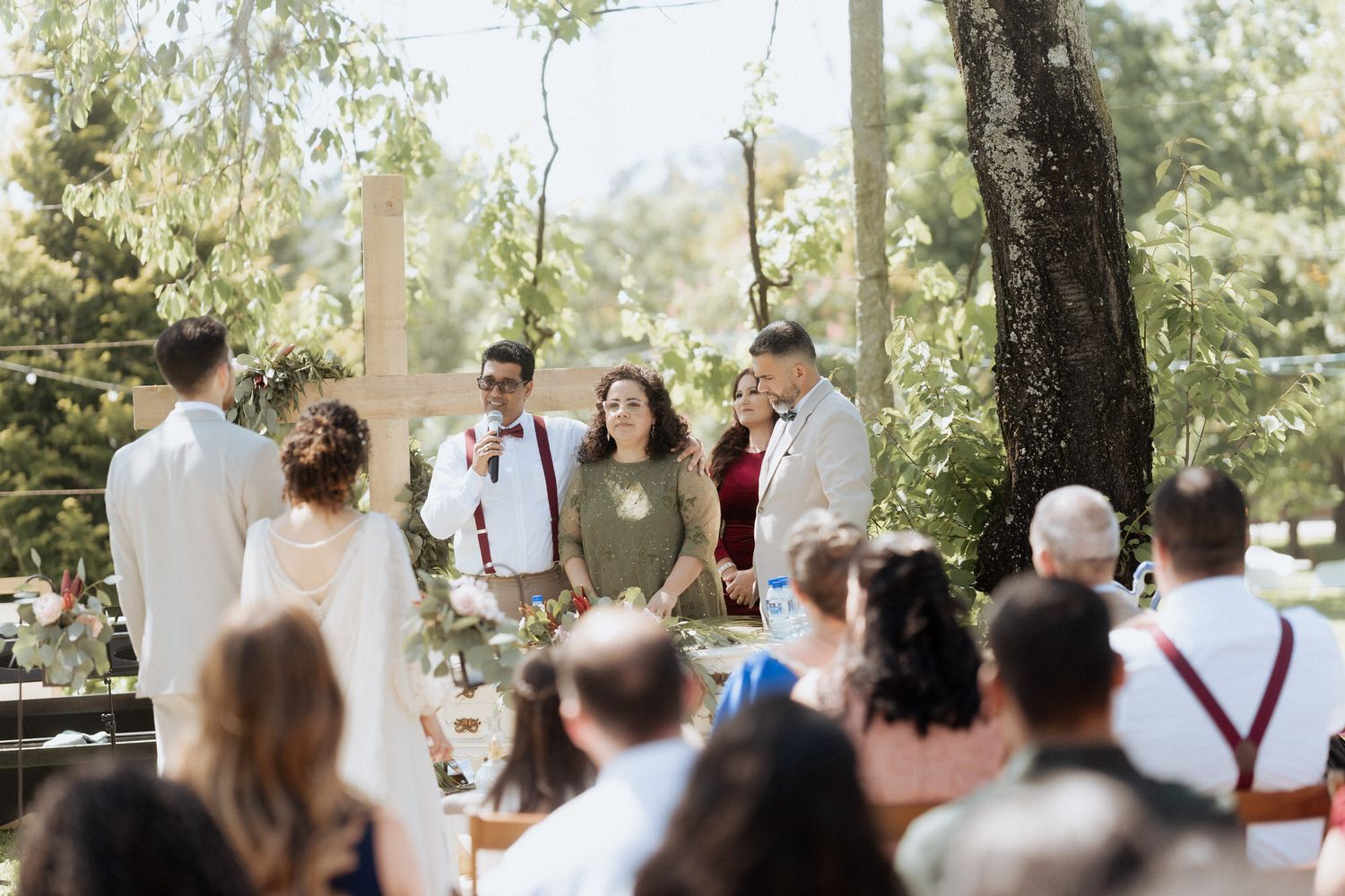 Wedding guests gather outdoors under trees for an intimate garden ceremony.