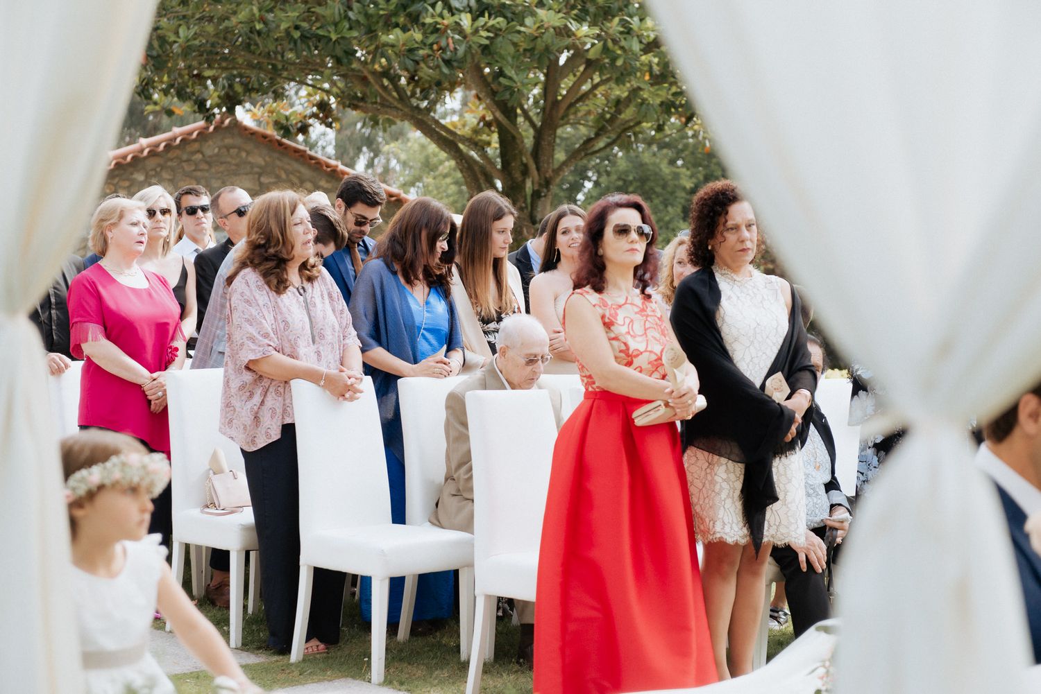 Wedding guests standing outside under white canopy tents at an outdoor reception celebration.